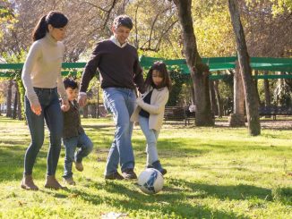 A family plays soccer together in a sunny park, enjoying quality time outdoors.